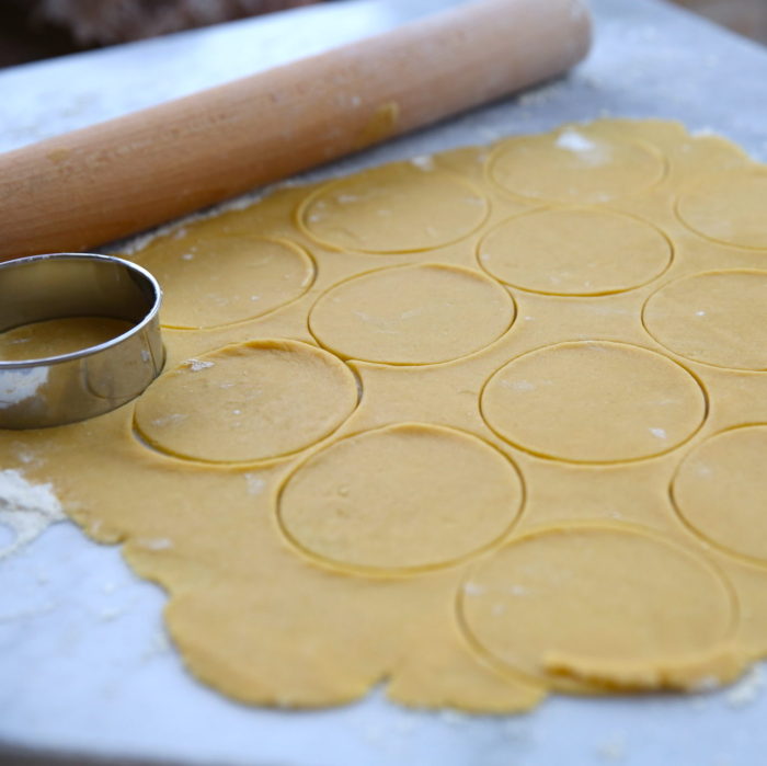 Einkorn pie dough rolled out with round hand-pie cutouts and a rolling pin on a floured surface