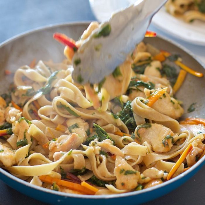 Gluten-free tagliatelle tossed with Prosecco chicken, rainbow chard, and heirloom carrots in a skillet
