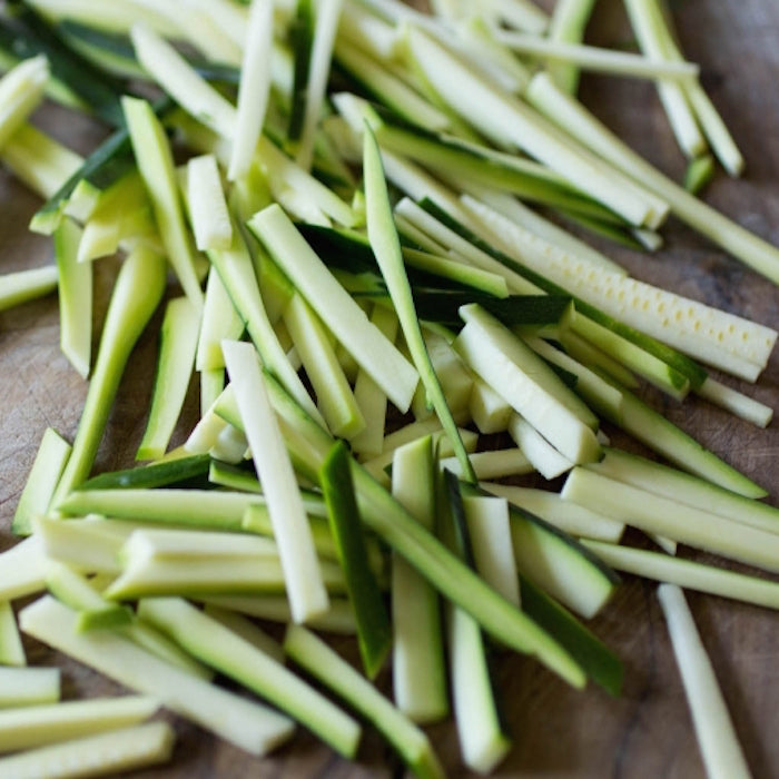 Julienned zucchini on a wooden cutting board, prepared for frying in a crispy zucchini recipe