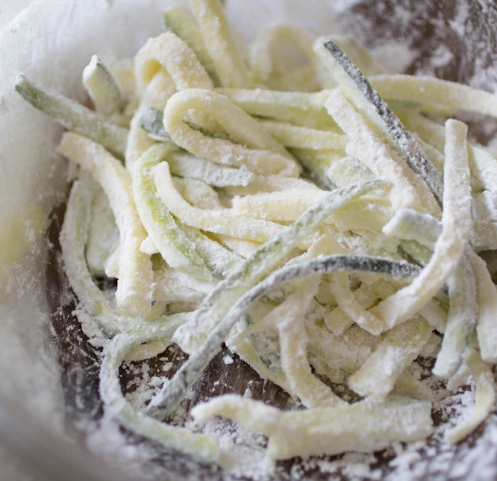 Zucchini strips coated in einkorn flour in a mixing bowl ready for frying