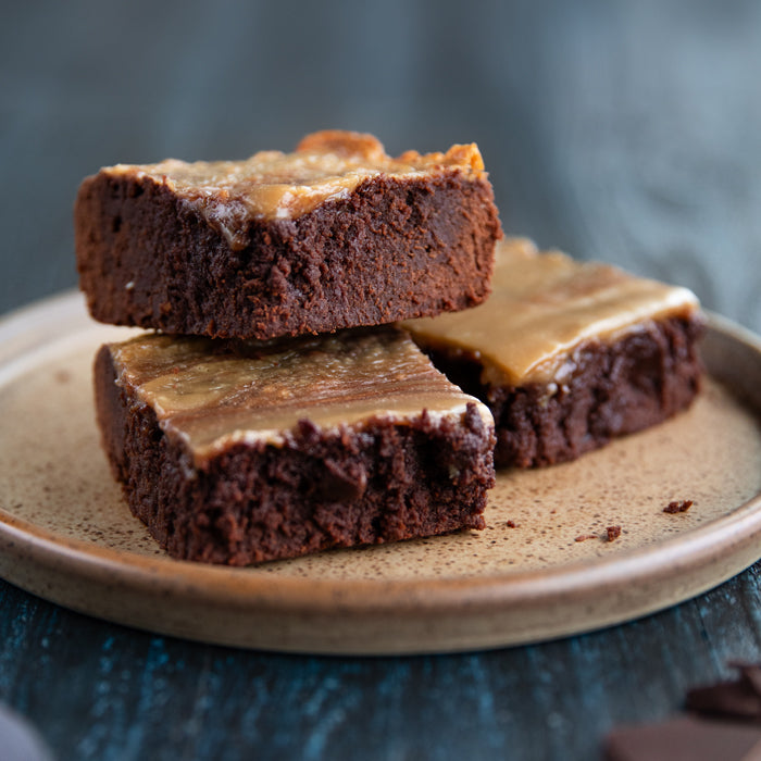 Close-up of three fudgy einkorn halva brownies on a ceramic plate, showing halva swirls and dense chocolate crumb