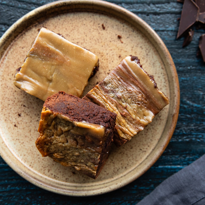 Overhead view of three fudgy Einkorn halva brownies showing swirled tahini halva topping on a speckled ceramic plate