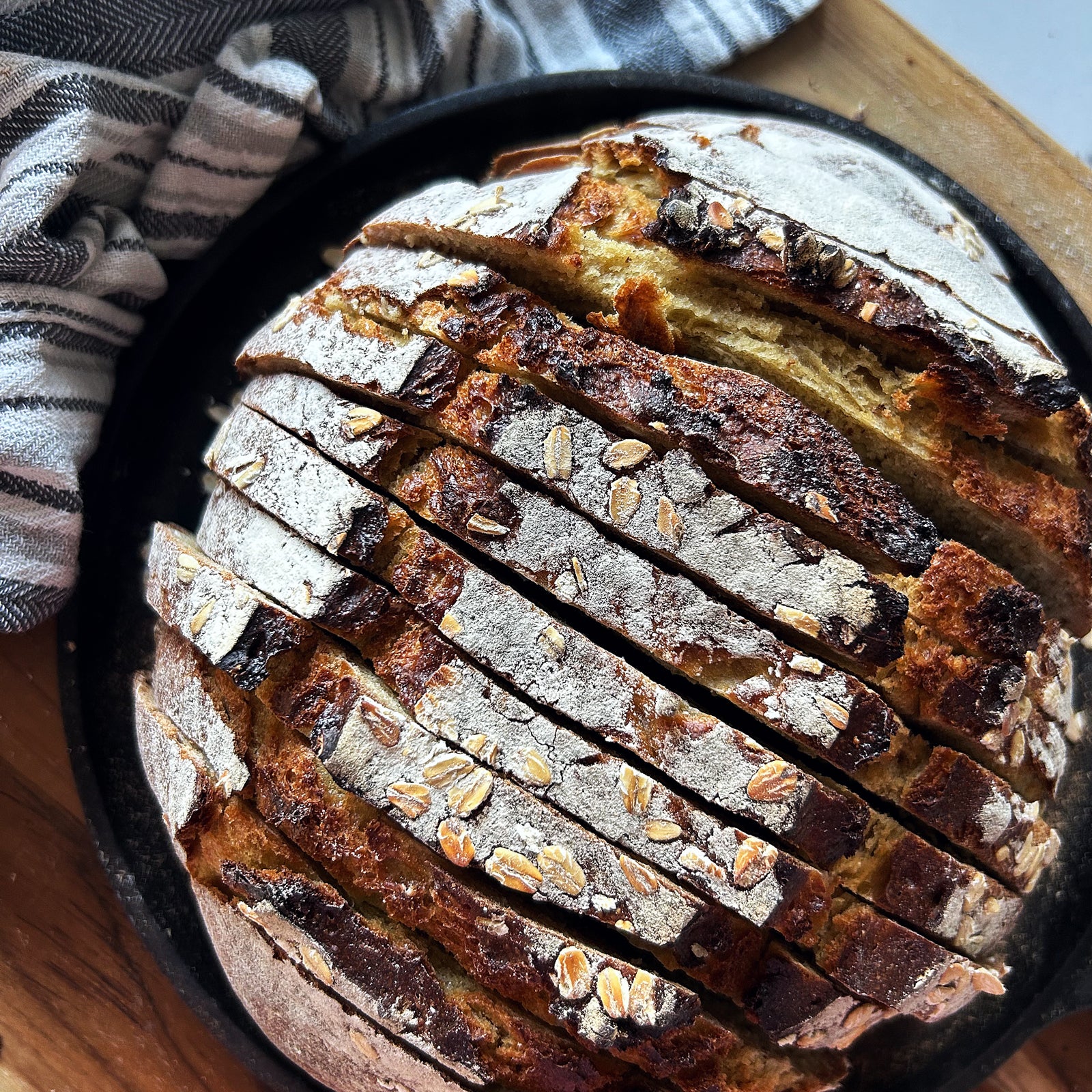 Close-up of sliced sourdough honey-oat einkorn boule showcasing golden crust, oat flakes, and airy crumb on a dark dish