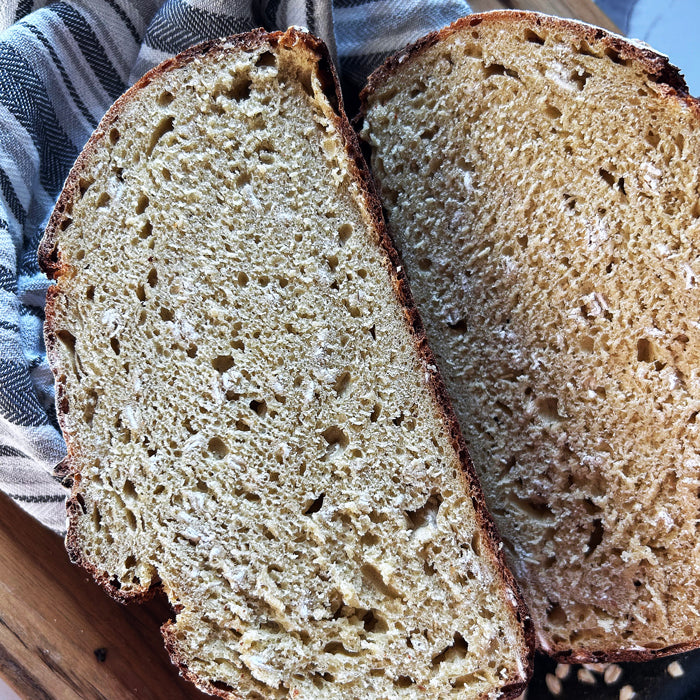 Top-down view of two slices of honey oat einkorn sourdough showing open golden crumb and crisp crust on a striped cloth