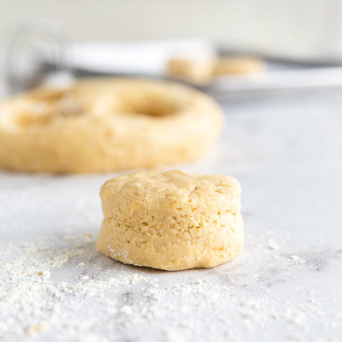 Front view of an unbaked Einkorn honey biscuit showing flaky layers on a floured marble countertop