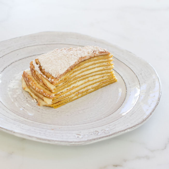 Side view of Einkorn pumpkin crepe cake slice with mascarpone layers, dusted with powdered sugar on a white plate