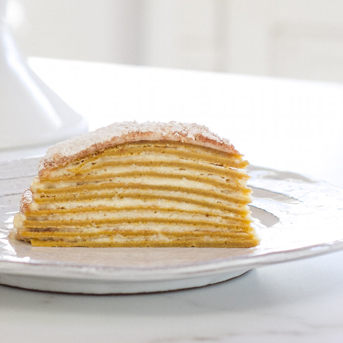 Side view of slice of Einkorn pumpkin crêpe mascarpone cake showing thin layered crêpes and cream filling on a white plate