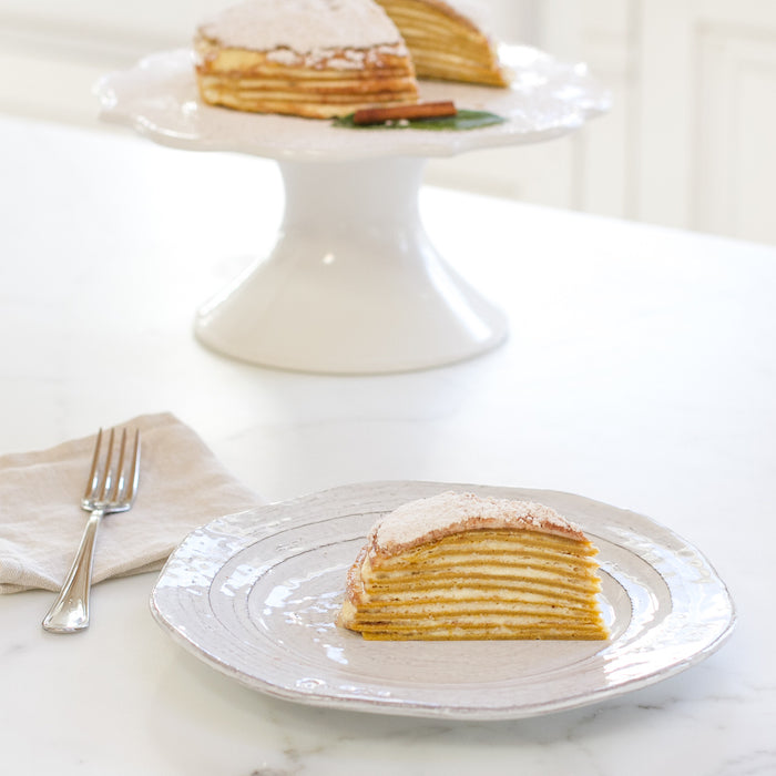 Side view of an Einkorn pumpkin crêpe mascarpone cake slice showing thin layered crepes dusted with powdered sugar on a white plate