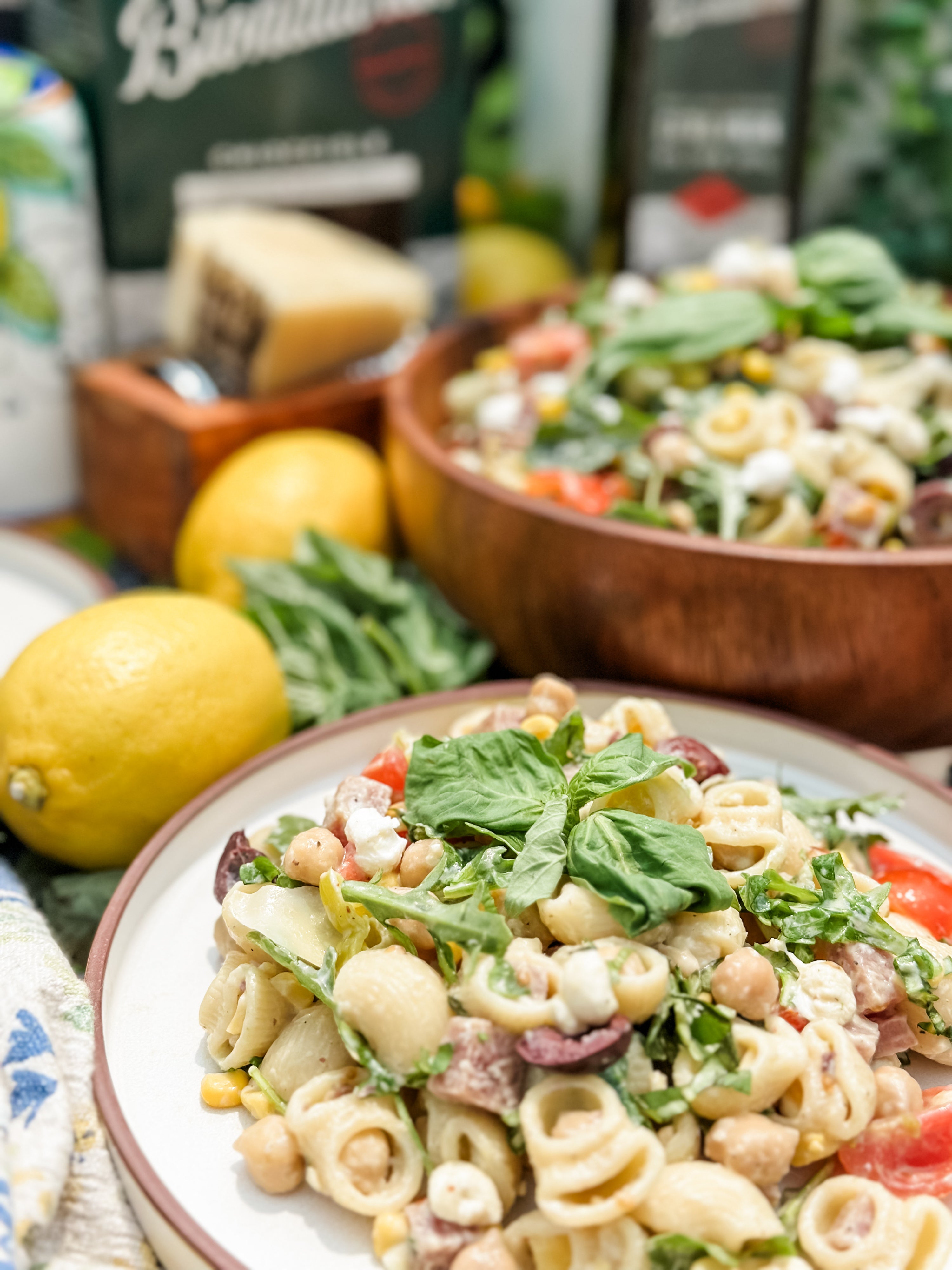 Creamy no-mayo pasta salad served on a plate garnished with fresh basil, lemons and a wooden serving bowl in the background