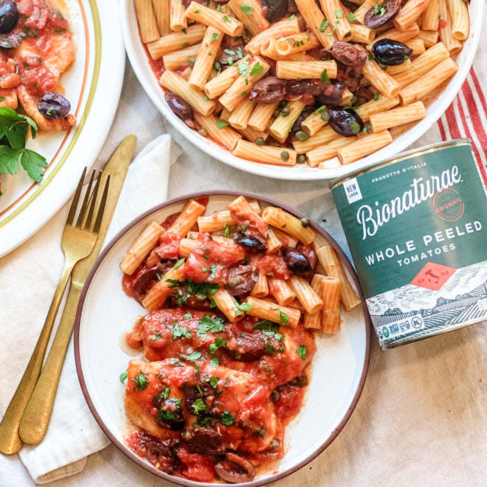 Chicken in tomato-caper sauce with penne and olives, garnished with parsley, can of Bionaturae Whole Peeled Tomatoes
