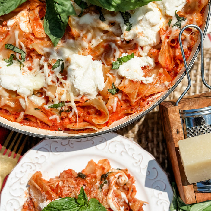 Italian skillet lasagna with melted ricotta and basil, plated beside a serving and a wedge of Parmesan on a woven mat