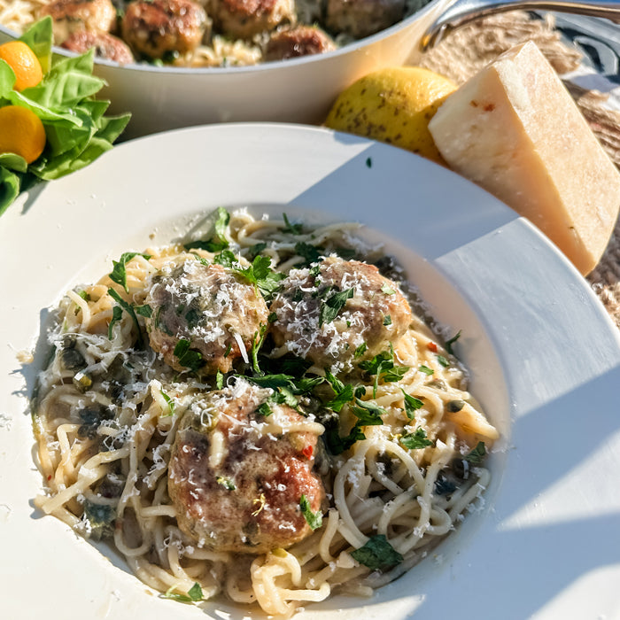 Close-up of plate with chicken meatballs in lemon-caper piccata sauce over capellini, topped with grated cheese and parsley