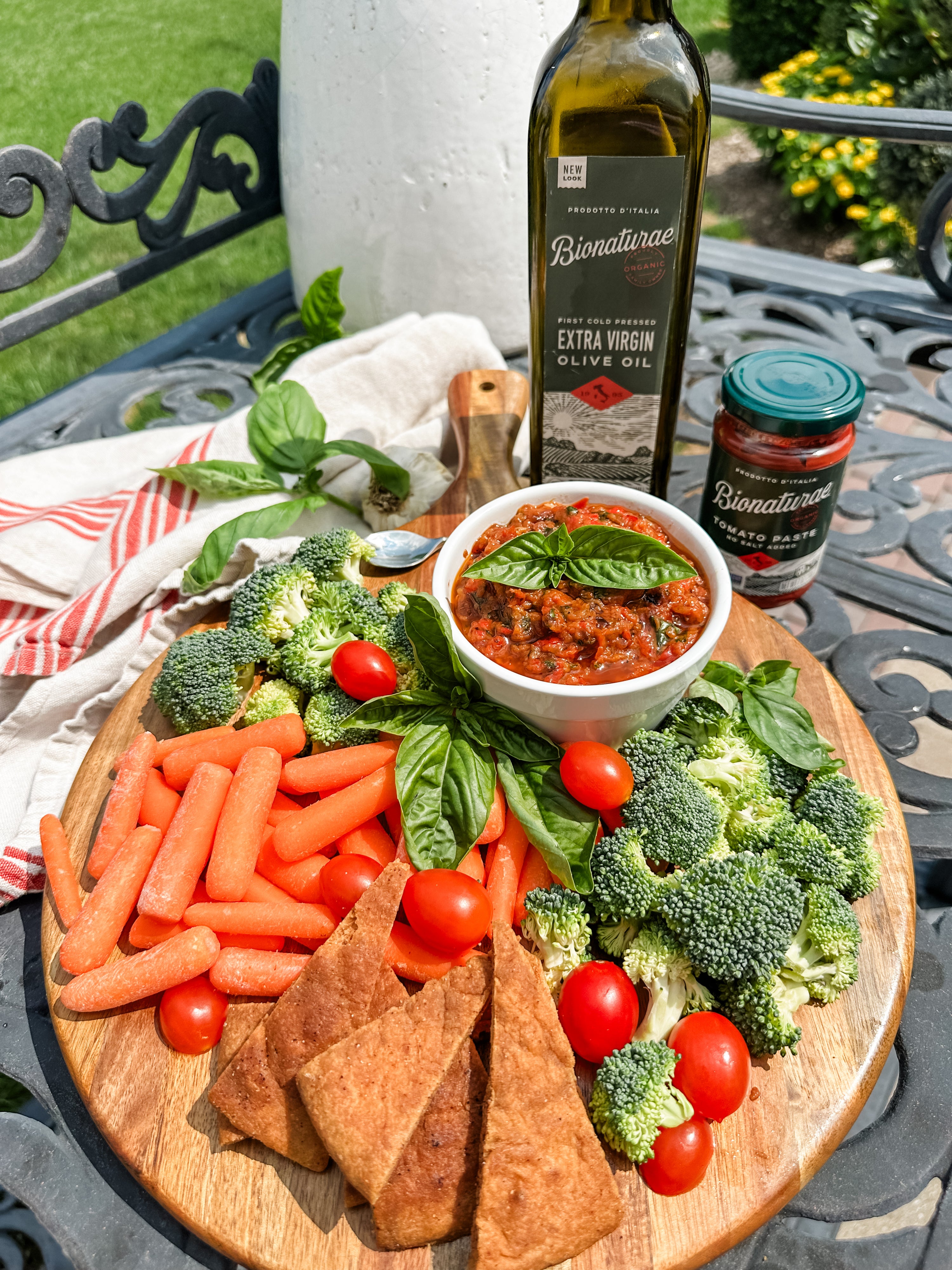 Roasted vegetable spread served with basil, baby carrots, broccoli, cherry tomatoes and pita chips on a wooden serving board