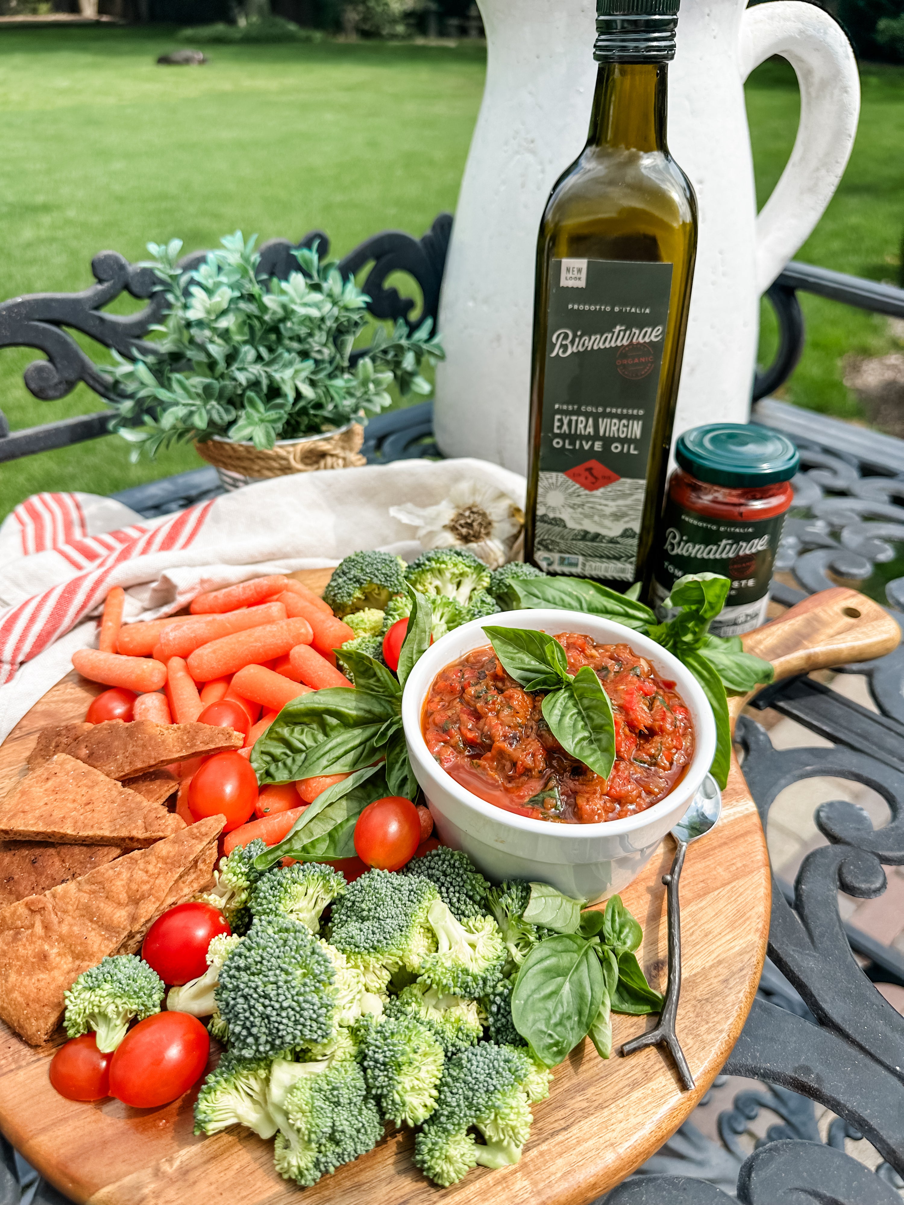 Roasted vegetable spread in a bowl with broccoli, cherry tomatoes, carrots, pita chips and organic olive oil outdoors