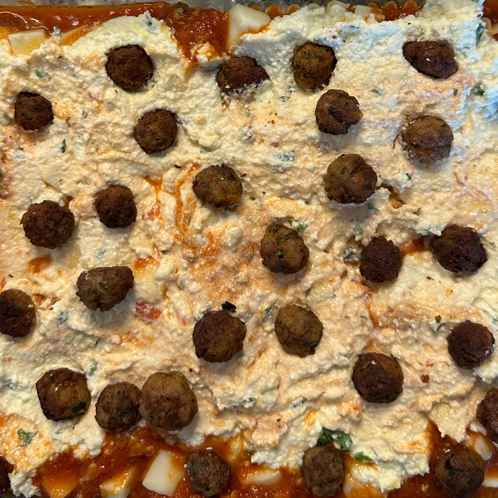 Neapolitan-style lasagna being assembled in a baking dish with a ricotta layer dotted with small meatballs over tomato sauce