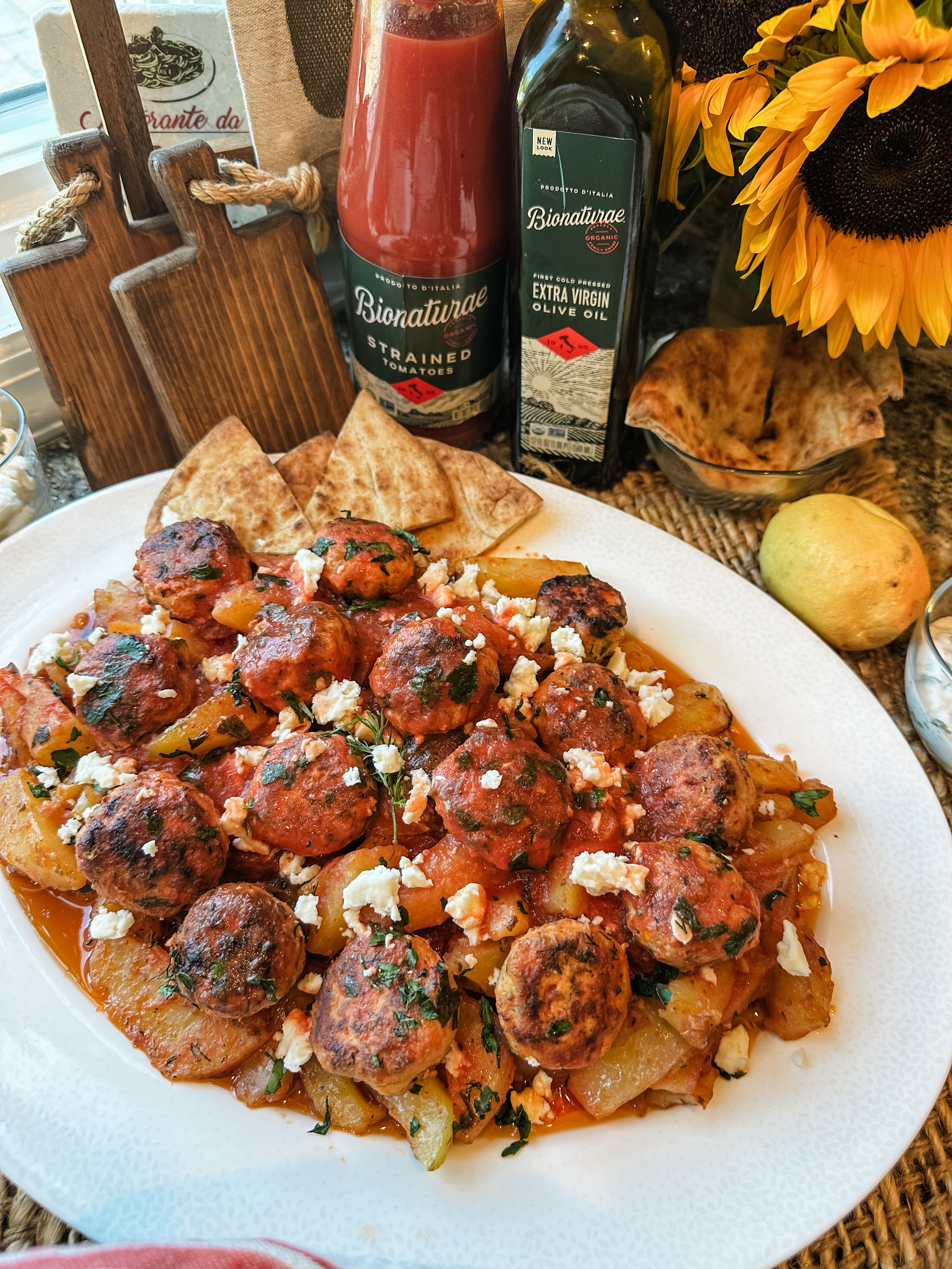Greek chicken meatballs with roasted potatoes on a white platter, topped with crumbled feta and pita wedges