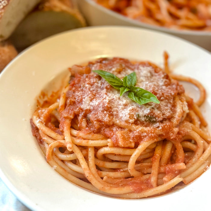 Close-up overhead view of bucatini amatriciana with tomato sauce, grated cheese and basil in a white bowl