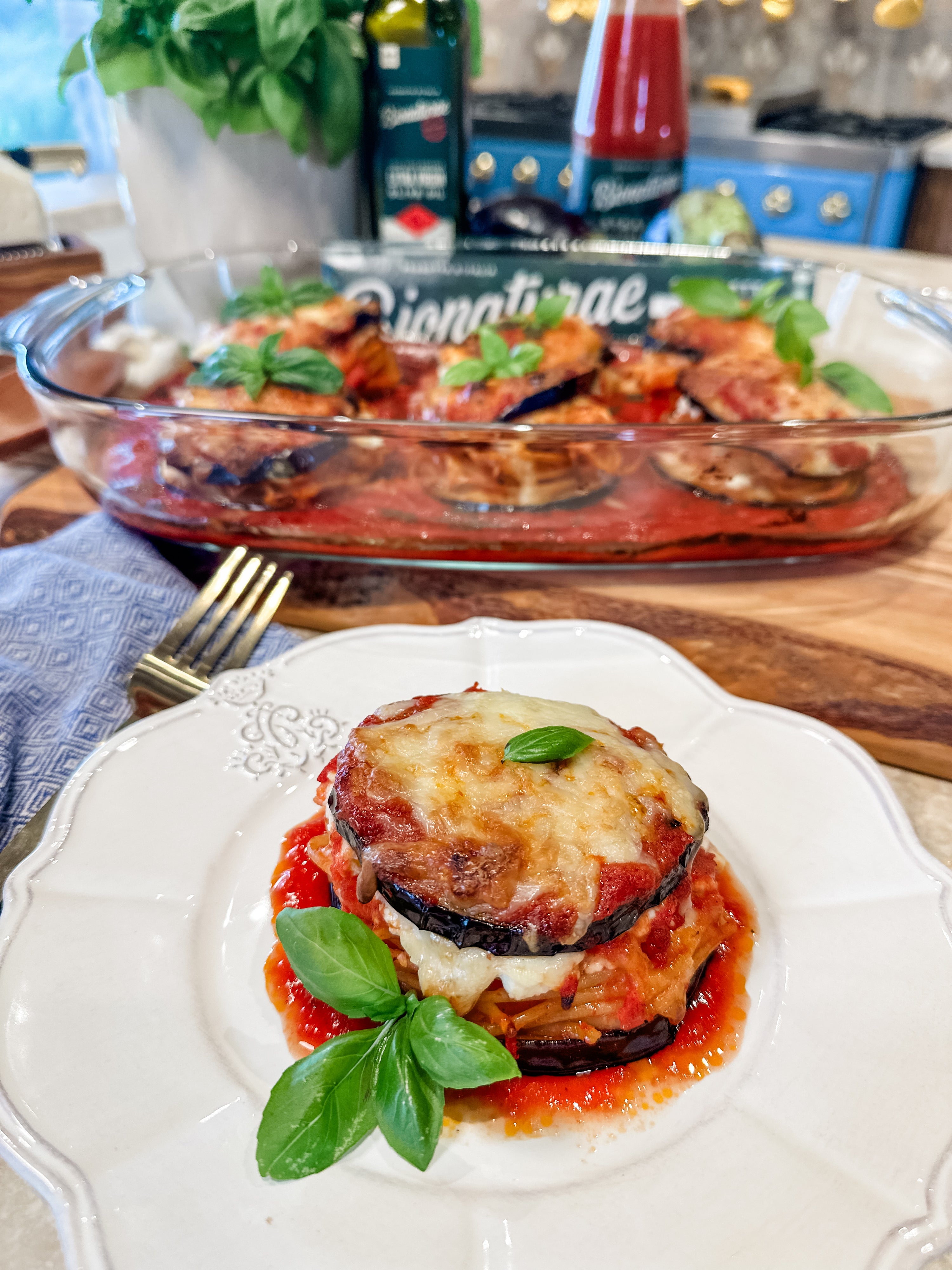 Stacked eggplant rounds filled with spaghetti and melted cheese, garnished with basil on a white plate with the baking dish in the background