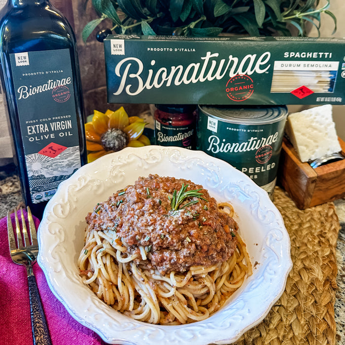 Bowl of meat-free mushroom bolognese over spaghetti with Bionaturae pasta box, canned tomatoes, and extra virgin olive oil in the background