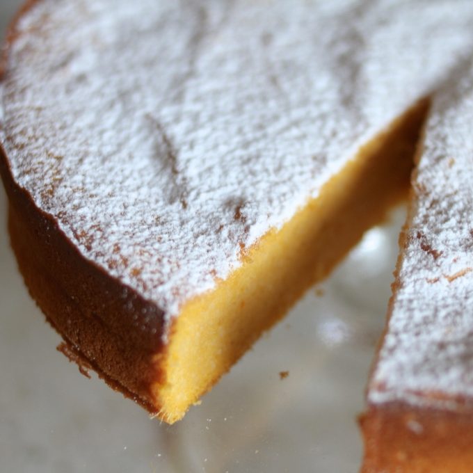 Close up of gluten free sweet potato sponge cake slice showing moist orange crumb and powdered sugar topping on a glass plate