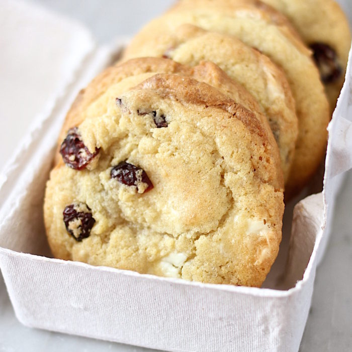 Close-up of einkorn cookies with white chocolate chunks and dried sour cherries in a paper tray