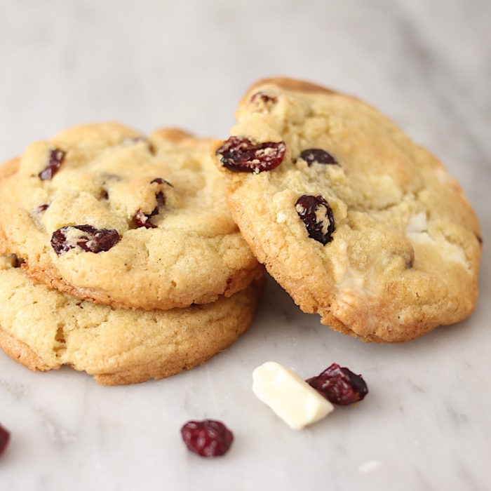 Close-up three-quarter view of sour cherry and white chocolate chunk Einkorn cookies showing dried cherries and white chocolate on a marble surface