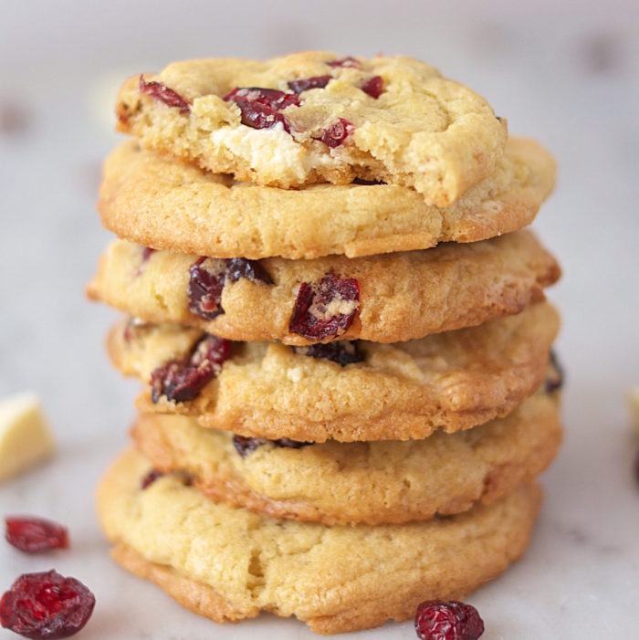 Stacked Einkorn cookies with white chocolate chunks and dried sour cherries, top cookie with a bite, marble background