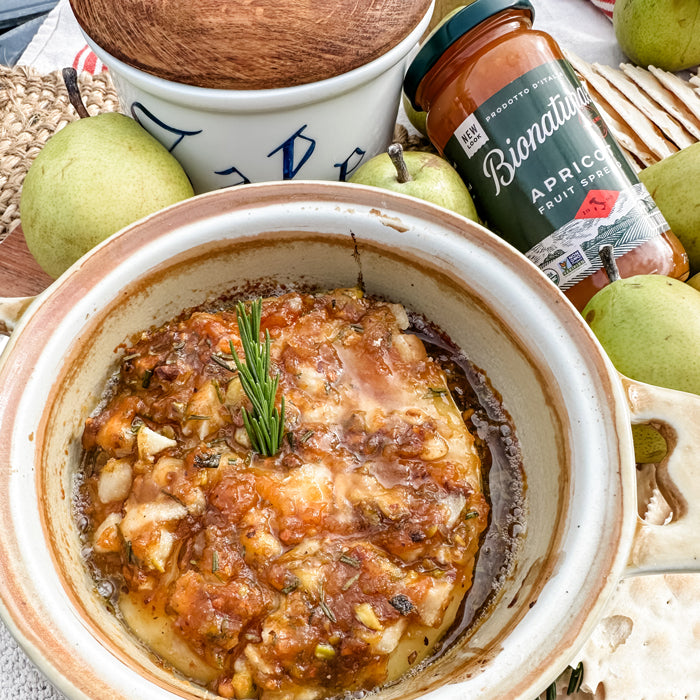 Baked Brie topped with Bionaturae Apricot Fruit Spread, chopped pears, pistachios, and rosemary in a ceramic baking dish