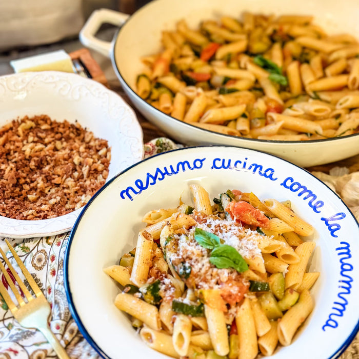 Penne with zucchini, tomatoes, basil, and grated cheese served in a bowl; rim reads ‘nessuno cucina come la mamma’