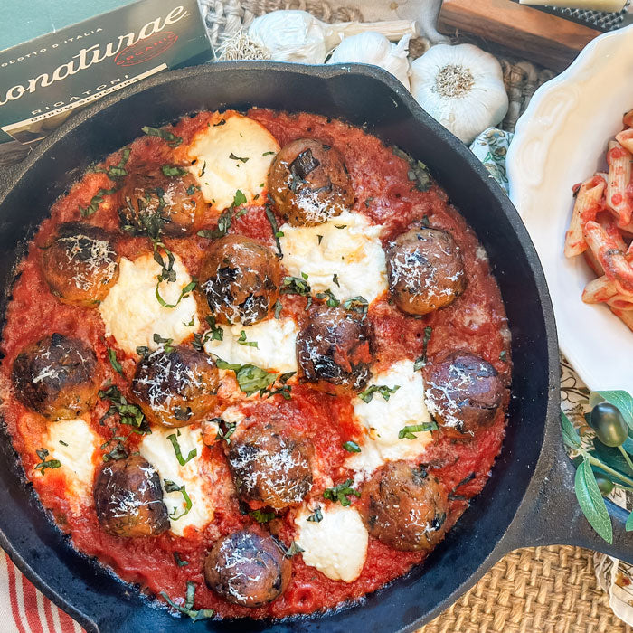 Skillet of baked eggplant meatballs in homemade marinara with dollops of melted ricotta, fresh basil, garlic, and a side of pasta
