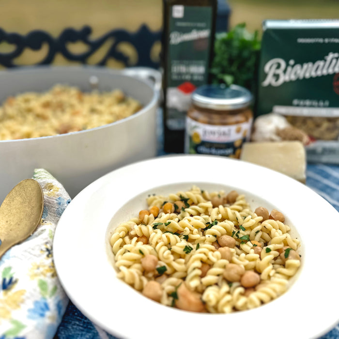 Bowl of fusilli pasta with chickpeas and parsley in a white bowl, casserole and Bionaturae products blurred in background
