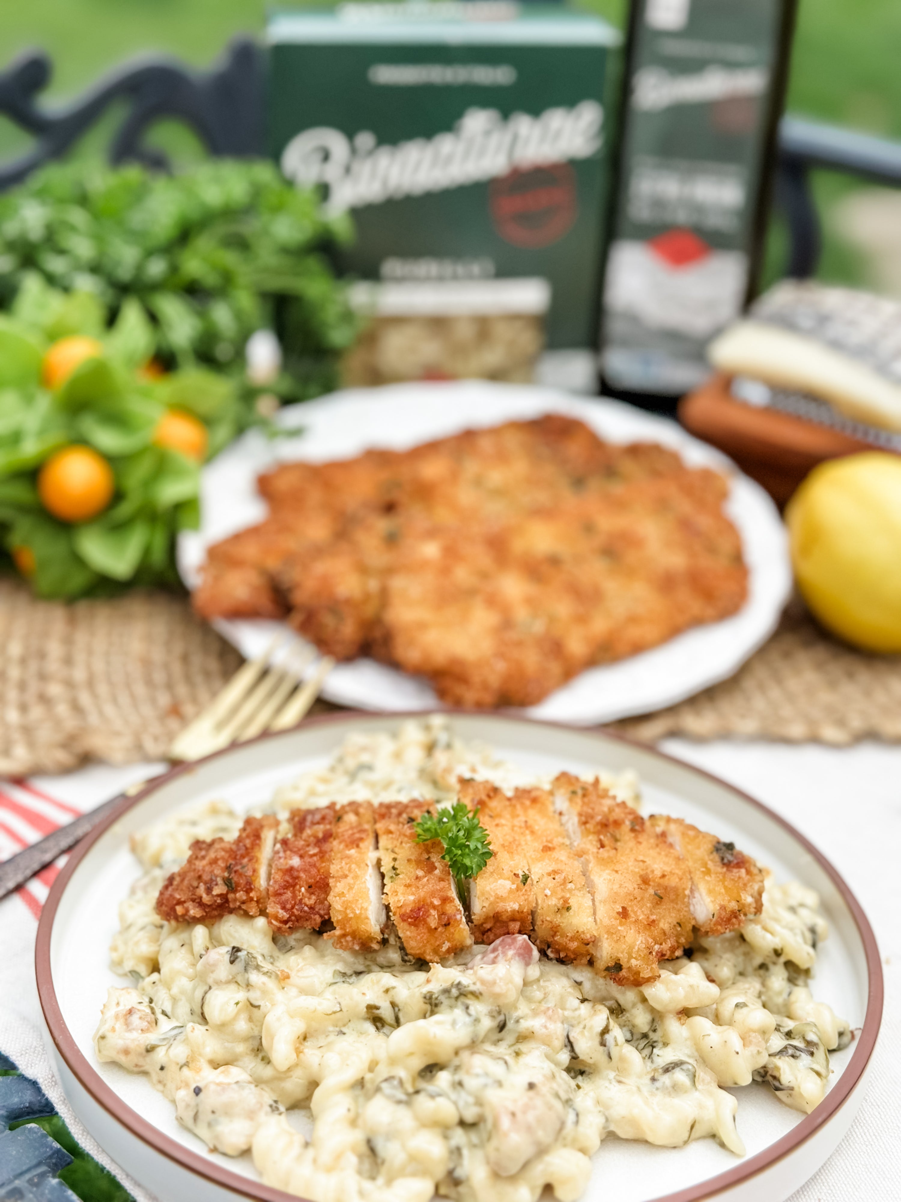 Close-up of creamy lemon Parmesan pasta with sliced crispy breaded chicken cutlet and parsley, blurred Bionaturae pasta box behind