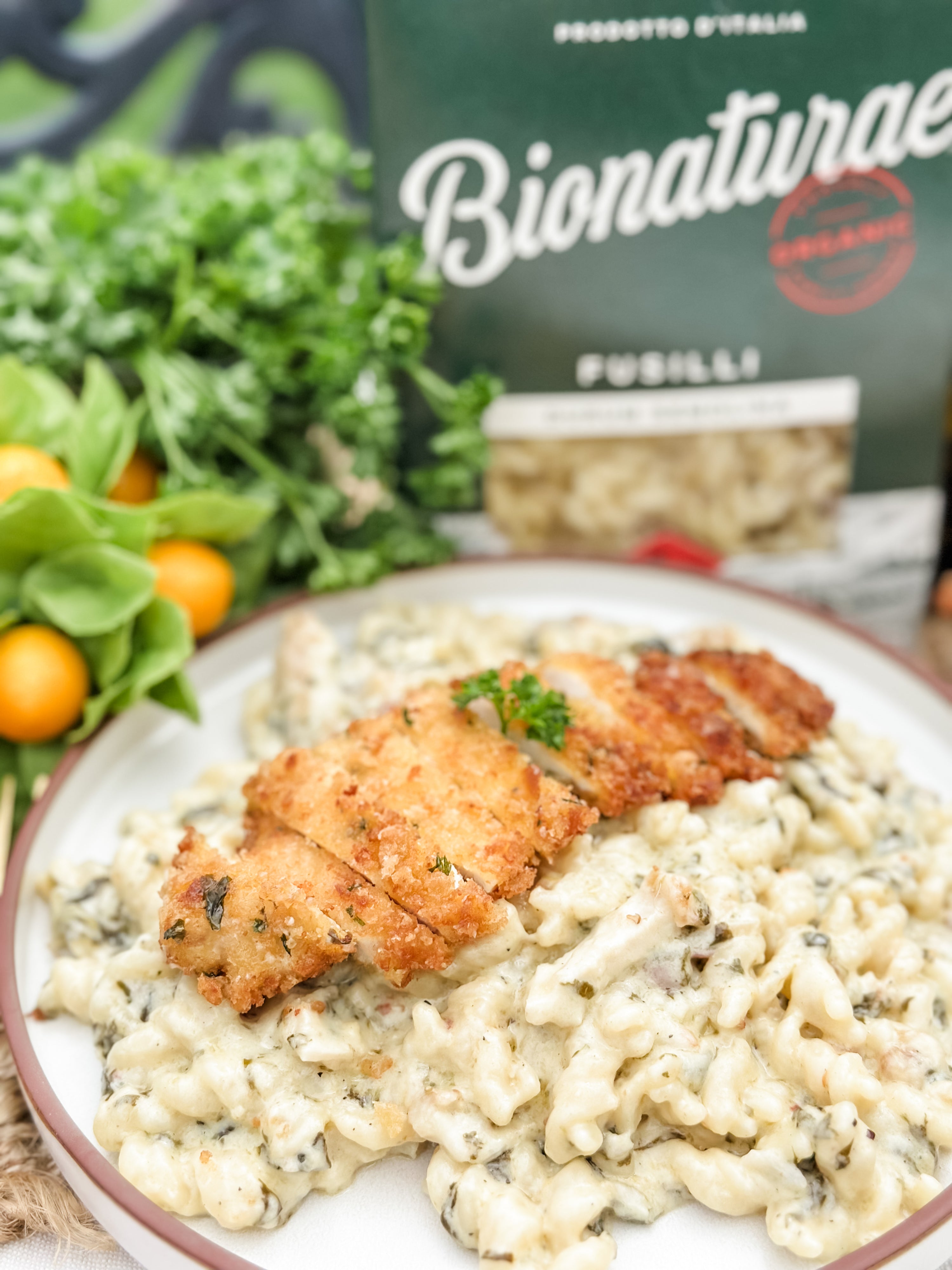 Breaded chicken cutlets over creamy lemon Parmesan fusilli pasta with herbs and Bionaturae pasta box in background