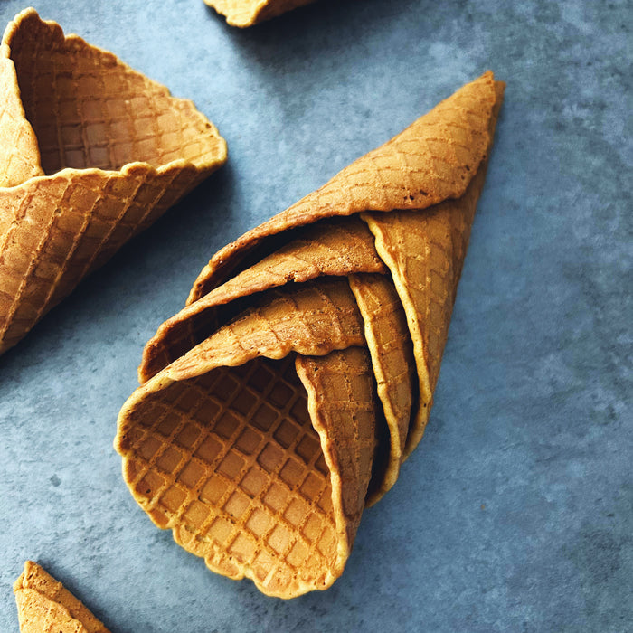 Overhead view of stacked Einkorn sourdough ice cream cones showcasing golden-brown color and waffle pattern on a blue-gray surface