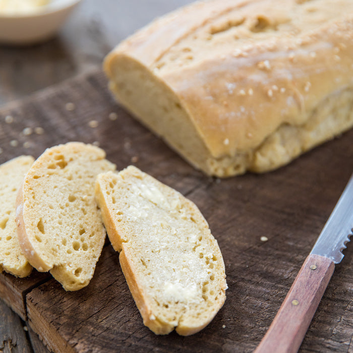 Close-up of sliced crusty Einkorn Italian bread showing open crumb and a buttered slice on a wooden cutting board