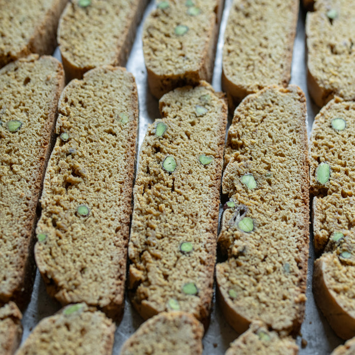 Top-down view of sliced einkorn pistachio biscotti showing crunchy golden texture and green pistachio pieces on parchment-lined tray