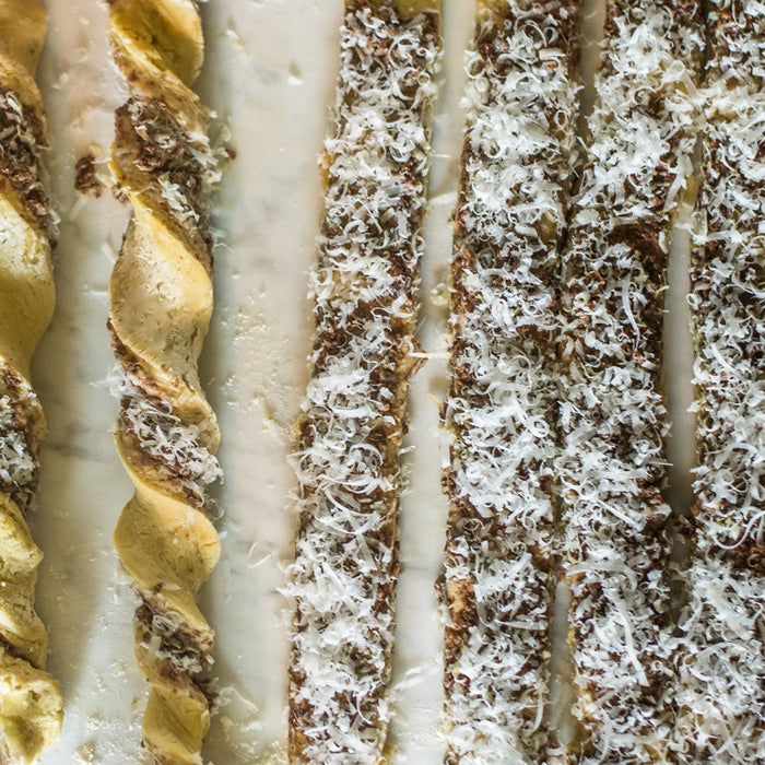 Top-down view of einkorn grissini spread with olive tapenade and sprinkled with grated cheese on parchment paper