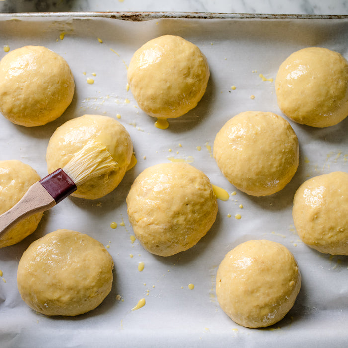 Einkorn maritozzi dough balls brushed with egg wash on a parchment-lined baking sheet
