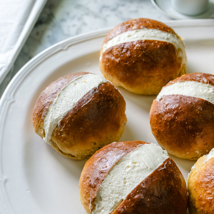 Close-up of four Einkorn Maritozzi buns showcasing a thick band of whipped cream on a white plate over a marble countertop
