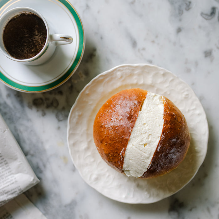 Einkorn maritozzo bun filled with cream on a white plate beside an espresso cup on a marble surface