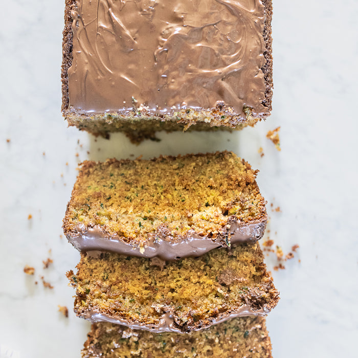 Top-down view of sliced rustic zucchini bread showcasing chocolate-hazelnut spread and visible zucchini flecks on a white marble surface