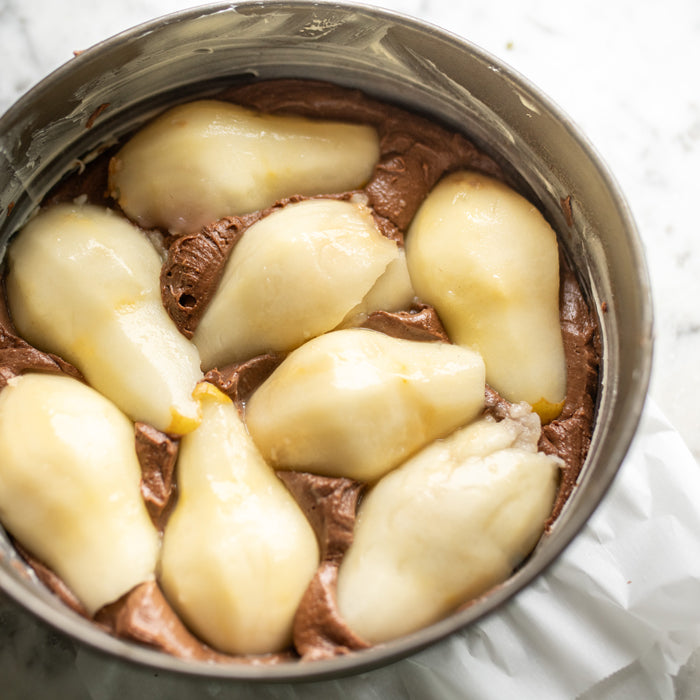 Top view of chocolate pear pudding cake in a round pan, halved poached pears arranged on chocolate batter