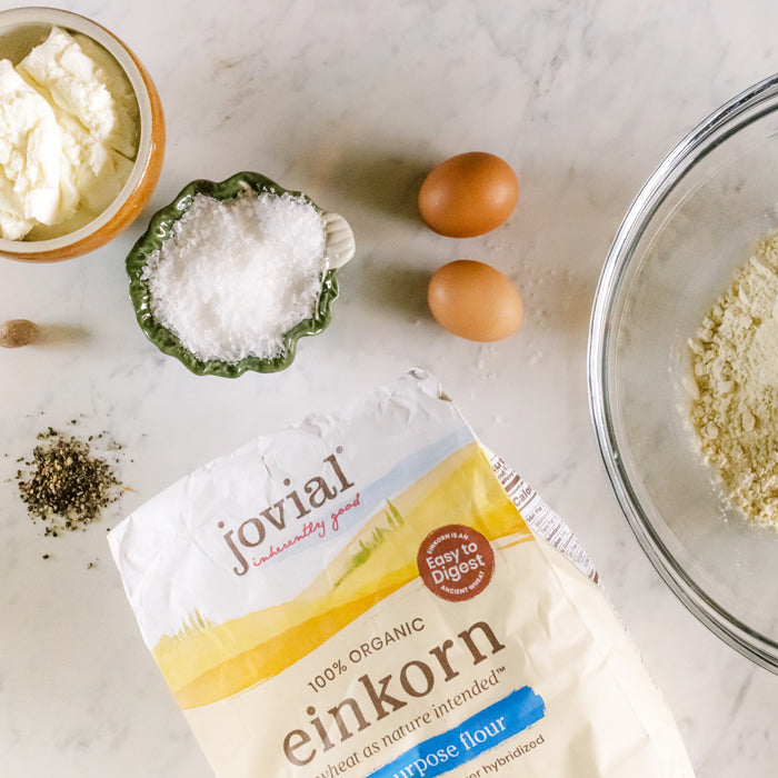Top-down of Jovial organic einkorn flour bag beside ricotta, eggs, salt, pepper, and a glass mixing bowl on marble