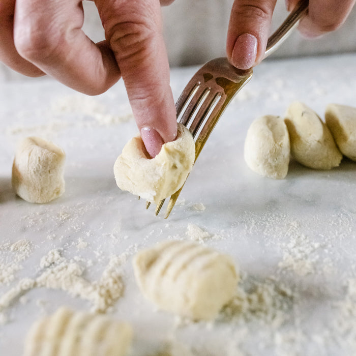 Hands shaping ricotta einkorn gnocchi with a fork on a floured surface