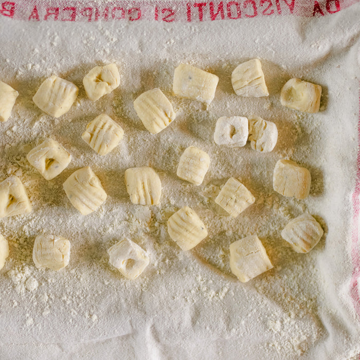 Top-down view of ricotta Einkorn gnocchi showcasing ridged, pillowy pieces dusted with flour on a floured kitchen towel