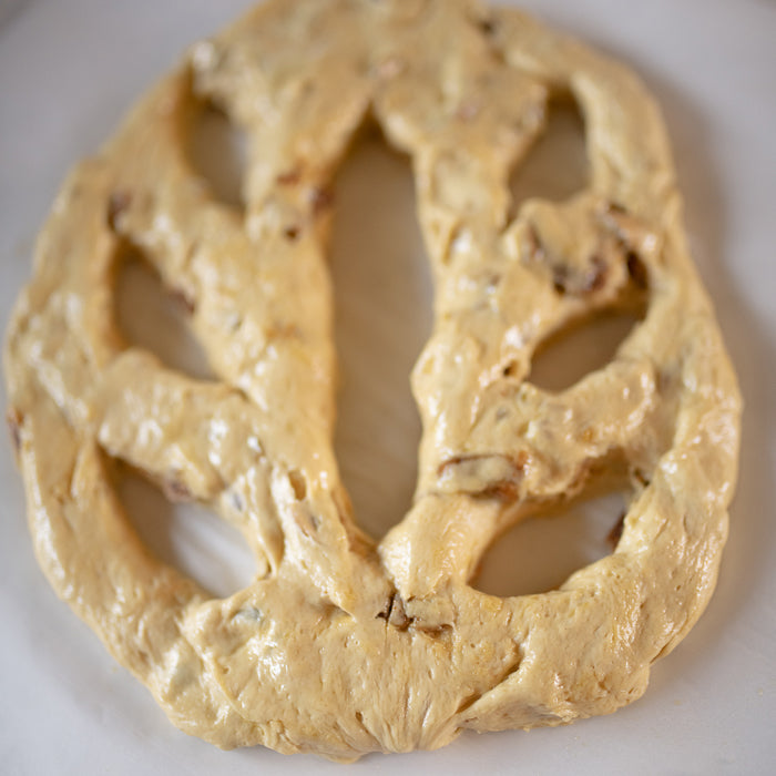 Top-down view of uncooked Einkorn breakfast loaf (fougasse) studded with figs and pistachios on a white surface