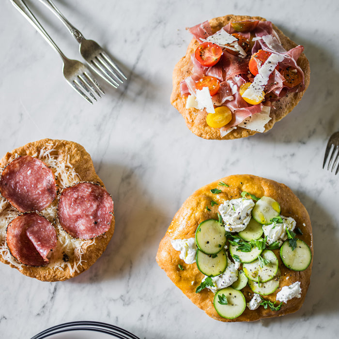 Three Einkorn mini pizza fritta on marble, prosciutto with cherry tomatoes, salami and cheese, zucchini with ricotta