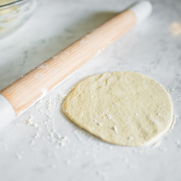 Einkorn dough disk being rolled on a floured marble countertop with a wooden rolling pin
