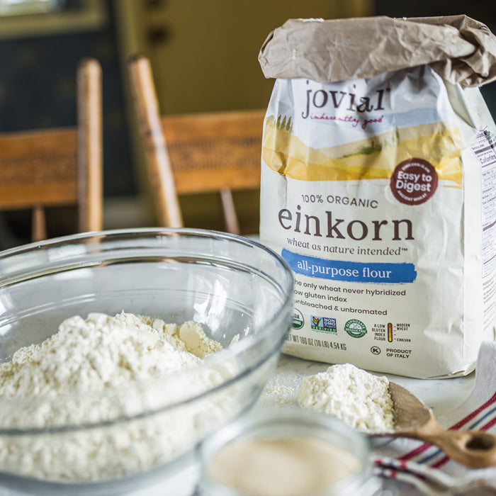 Front-left view of Jovial organic einkorn all-purpose flour bag showcasing the package label with a glass bowl of flour on a kitchen table