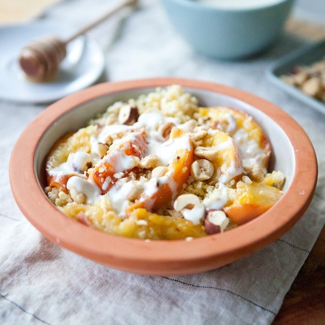 Gluten-free millet breakfast bowl with caramelized peaches, honeyed yogurt, and toasted hazelnuts on a linen napkin